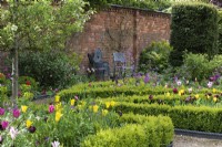 View across box edged beds filled with tulips, towards a sheltered seating space beside a cistern panel lead fountain.
