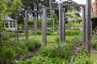 Oak frames straddle a path that meanders through a contemporary garden with circular lawns, and borders planted with alliums, geums and leafy perennials to flower later.