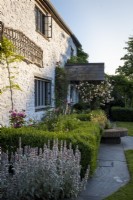 Old Welsh stone cottage with tiled porch, rosa 'New Dawn' climbing over, and cottage style planting with a formal hedge parterre