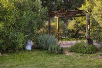 Mediterranean garden view with a wooden gazebo with table and chairs among greenery including Oleander tree, Lavandula and decorative elements as white balls. 
Italy, Tuscan Maremma, Orbetello
Autumn season, October
