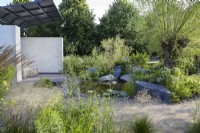 Cancer Research UK Legacy Garden. Seating area in the Pledge Pavillion. Pathway around rocky island border with Salix, hostas, grasses and Tanacetum. Summer.