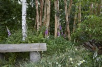 Wooden seat in wildlife garden with wildflowers and posts resembling trees that have been drilled with different sized holes for insects and other creatures to use. Summer.