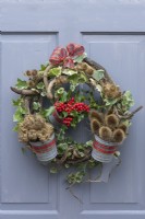 The Holly and the Ivy Wreath. Twisted twigs and ivy stems are wound round a metal frame and secured with wire. It is adorned with ivy, whilst three small buckets are filled with seasonal plant material.