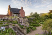 View over the garden with a wooden arbour with Wisteria and stone steps down to the gravel garden with mixed perennial planting 
