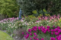 Sculpture 'Vita' by 'Vicki Atkinson', seen over deep pink Tulipa 'Barcelona' and pink and white 'Dreamland. To right, Tulipa 'Menton'.