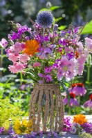 Summer bouquet with sweet peas, roses, monarda, pot marigold, echinops, persicaria and poppy in home made vase made of  glass jar and paper rope.