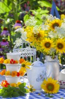 Table arrangement with a bouquet of sunflowers, teapot, self made stand of teacups and saucers decorated with pot marigold and nasturtium flowers.