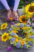 Woman making summer wreaths with sunflowers, pot marigold, fennel, globe thistles, wild carrots, coneflowers and bergamot.