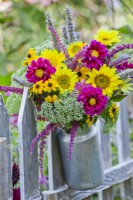 Summer bouquet containing sunflowers, sedum, dahlia, rudbeckia, agastache and amaranthus in a milk churn hanging from fence.