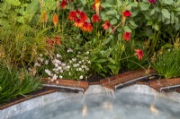 Copper metal rills with water flowing into a small pool - late summer mixed perennial planting of Echinacea 'Eccentric', Kniphofia 'Papaya Popsicle', Bulbine frutescens Avera Sun Series Sunset Orange, Panicum virgatum 'Squaw' and Erigeron 'Lavender Lady' - Mexican Fleabane 