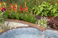 Copper metal rill with water flowing into a raised small pool - late summer mixed perennial planting of Echinacea 'Eccentric', Dahlia 'Black Narcissus', Kniphofia 'Papaya Popsicle'