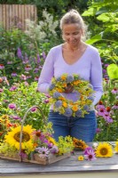 Woman making wreath using pot marigold, fennel, coneflower, globe thistles and wild carrots.