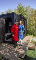 Portrait of garden designer Taina Suonio with a Chelsea pensioner on press day on a timber wooden deck - black painted wood sauna cabin 