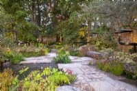 Reclaimed stone paving and mixed perennial in a new urban garden with benches, pond and pipe sculpture