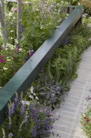 Landform Mental Wealth Garden. Designer: Nicola Hale. Metal 'rail' feature surrounding border with herbs edging pathway.Summer.