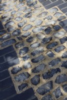 Mottled shadows over pathway of inlaid flint edged with black bricks.