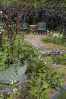 The Traditional Townhouse Garden. Designer: Lucy Taylor. Prunus serrula - Tibetan Cherry - and Athyrium niponicum Metallicum with Alchemilla mollis are potted within the border. Knapped flint edged pond with seating behind. Summer.