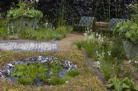 The Traditional Townhouse Garden. Designer: Lucy Taylor. Seating area by round pond edged with knapped flint bordered by a carpet of sedum. Aquatic plants include Pontederia cordata - pickerel weed - and Pistia stratiotes - water lettuce. Summer.