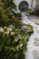 The Lunar Garden Designer: Queenie Chan. Low bamboo fence by white themed border with white gravel and white wall containing round antique mirror glass.