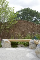 Inghams Working with Nature Garden. Designers: Joshua Parker and Matthew Butler. Seating area. Beams of wood inlaid on rock to form seats. Large willow screen for garden privacy. Summer.