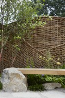Inghams Working with Nature Garden. Designers: Joshua Parker and Matthew Butler. Seating area. Beams of wood inlaid on rock to form seats. Large willow screen for garden privacy. Summer.