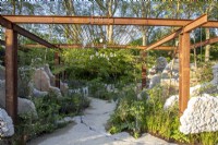 Modern contemporary garden made with salvaged building materials - rusty steel girder pergola - reclaimed concrete garden path and sculpture - mixed perennial planting including rare Aralia chapaensis