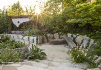 Modern contemporary garden made with salvaged building materials -reclaimed concrete steps down to seating area with an oak bench seat - mixed perennial planting by steps of Libertia Chilensis Grandiflora and Acanthus mollis Latifolius Group 'Rue Ledan' 
