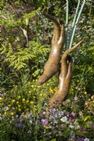 Bronze otters sculpture by Simon Gudgeon with mixed perennial planting of Lychnis flos-cuculi and Ranunculus acris 