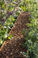 Laser cut corten steel dead hedge for filling with garden prunings that create habitats for beneficial insects surrounded by mixed perennial planting and wildflowers 