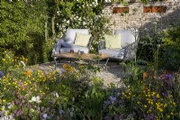 Patio seating area with table and chairs, mixed perennial planting of Geranium, Lychnis flos-cuculi, Ranunculus acris, Trollius chinensis,
Viburnum opulus and drystone wall with corten steel nesting boxes 