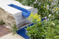A modern contemporary water rill made from recycled plastics set in stone - mixed perennial planting Euphorbia robbiae, Geranium pratense 'Mrs Kendall Clark' and Lychnis flos-cuculi 