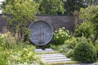 Garden wall made from stacked concrete slabs,circular water feature with brass taps, mixed perennial planting in white and green colours including Hydrangea arborescens 'Annabelle'