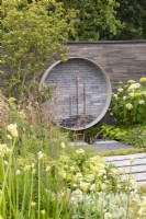 Garden wall made from stacked concrete slabs with a circular water feature with salvaged brass taps, mixed perennial planting in white and green colours