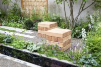 Wooden cube seats in a gravel garden surrounded by mixed perennial planting including Delphinium 'Guardian White', Brunnera macrophylla 'Jack Frost', Geranium wallichianum 'Azure Rush'