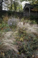 Deep autumnal beds at The Garden House, Devon. Grasses and late flowering perennials drift through each other with summerhouse at the back