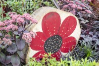 A tree stump made into an insect hotel with a painted poppy flower for decoration, planting of Sedum