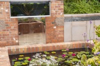A raised pond with red brick surround, planted with Nymphaea 