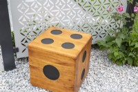A wooden domino cube seat on a gravel surface with a stainless steel laser cut patterned screen 