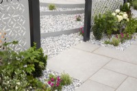 Stone paving leading to a gravel area with steps - a laser cut stainless steel patterned screen - mixed perennial planting in a gravel border 