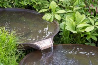 A round corten steel bowl with a spout flowing into another bowl  