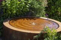 A round corten steel water feature with planting of Rosmarinus officinalis and Mentha - Mint