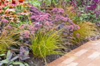 Border with mixed perennial planting,  Carex testacea 'Prairie Fire' and Sedum in flower 