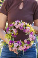 Woman holding summer wreath made of mostly pink flowers including Echinacea, Rosa, Fennel, Monarda and Veronicastrum.
