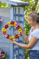Person hangs summer flower wreath made of Dahlia, Helianthus, Foeniculum, Calendula, Petunia, Sweet peas and Guelder rose berries.