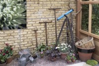 Tools and equipment against a brick wall in a wooden greenhouse, June