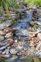 A stream cascading over stone rocks into a pond 