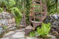 A rusty spiral staircase, stone paving and a low retaining wall, planting of Osmunda regalis - Royal fern and Matteuccia struthiopteris at the base 