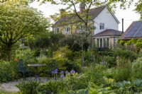 Elegant metal garden furniture in quiet spot amongst summer flower borders, with large house behind