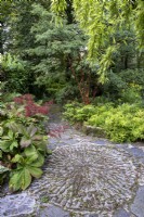 Decorative cobbled circular area, in a shady and lush autumnal garden