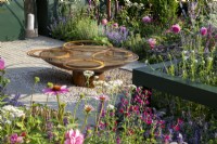 Reclaimed circular corten steel metal water feature with rusty hoops, mixed perennial planting flowerbeds of Salvia, Echinacea and Rosa 'Princess Alexandra of Kent' syn. 'Ausmerchant'